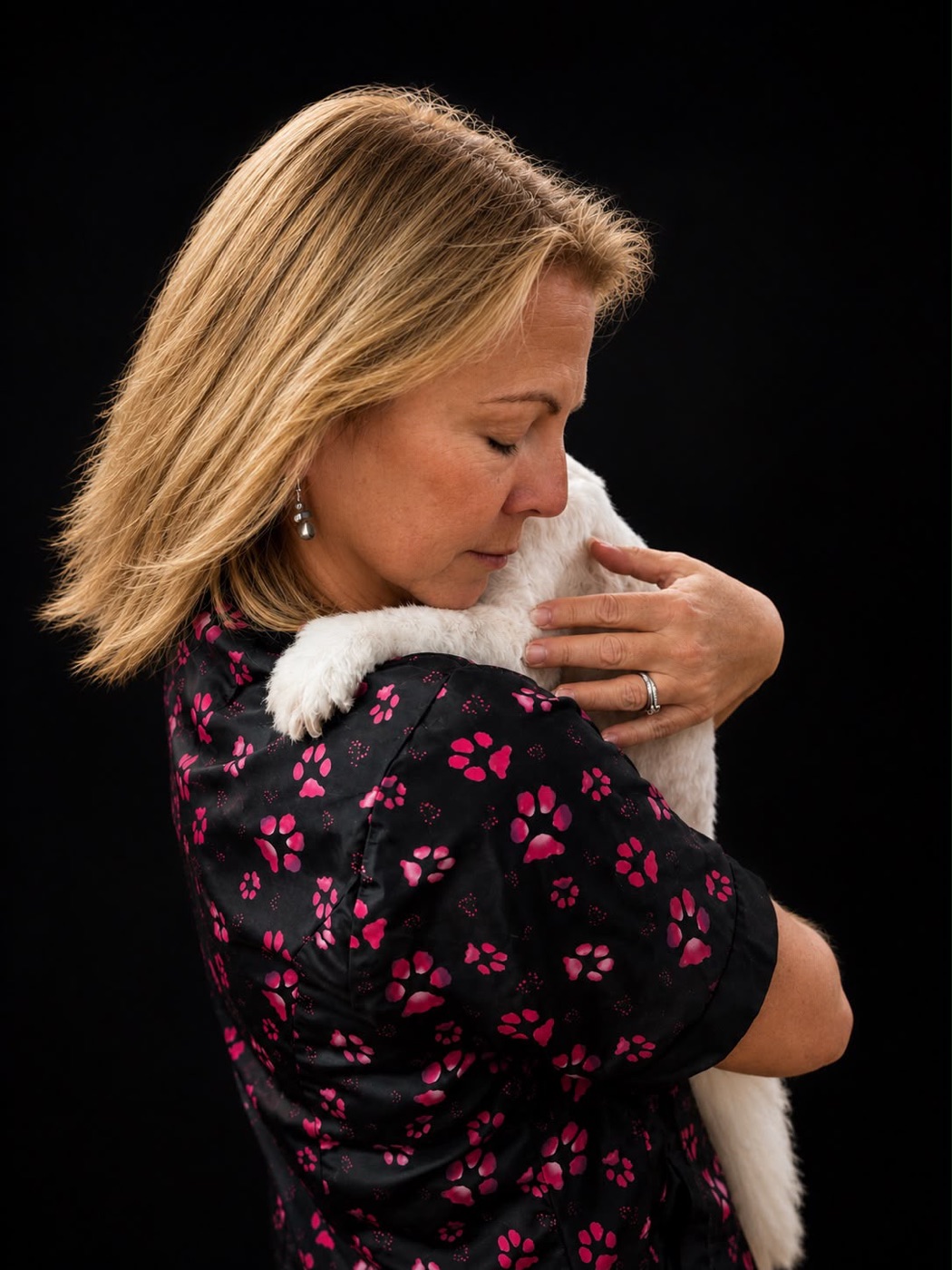 Groomer cuddling a small white dog over her shoulder
