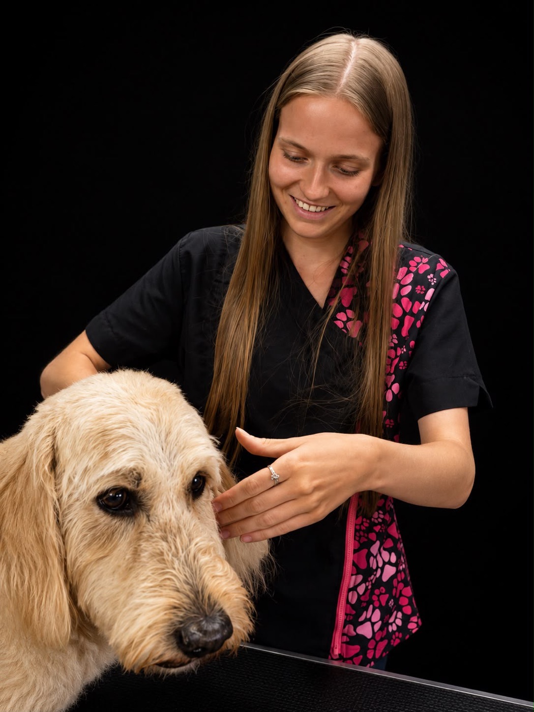 A smiling groomer settling a happy doodle at the grooming table